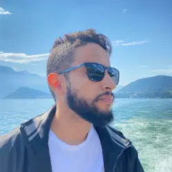 A picture of me smiling, wearing a blue t-shirt and a stone collar with some coconut trees behind me.